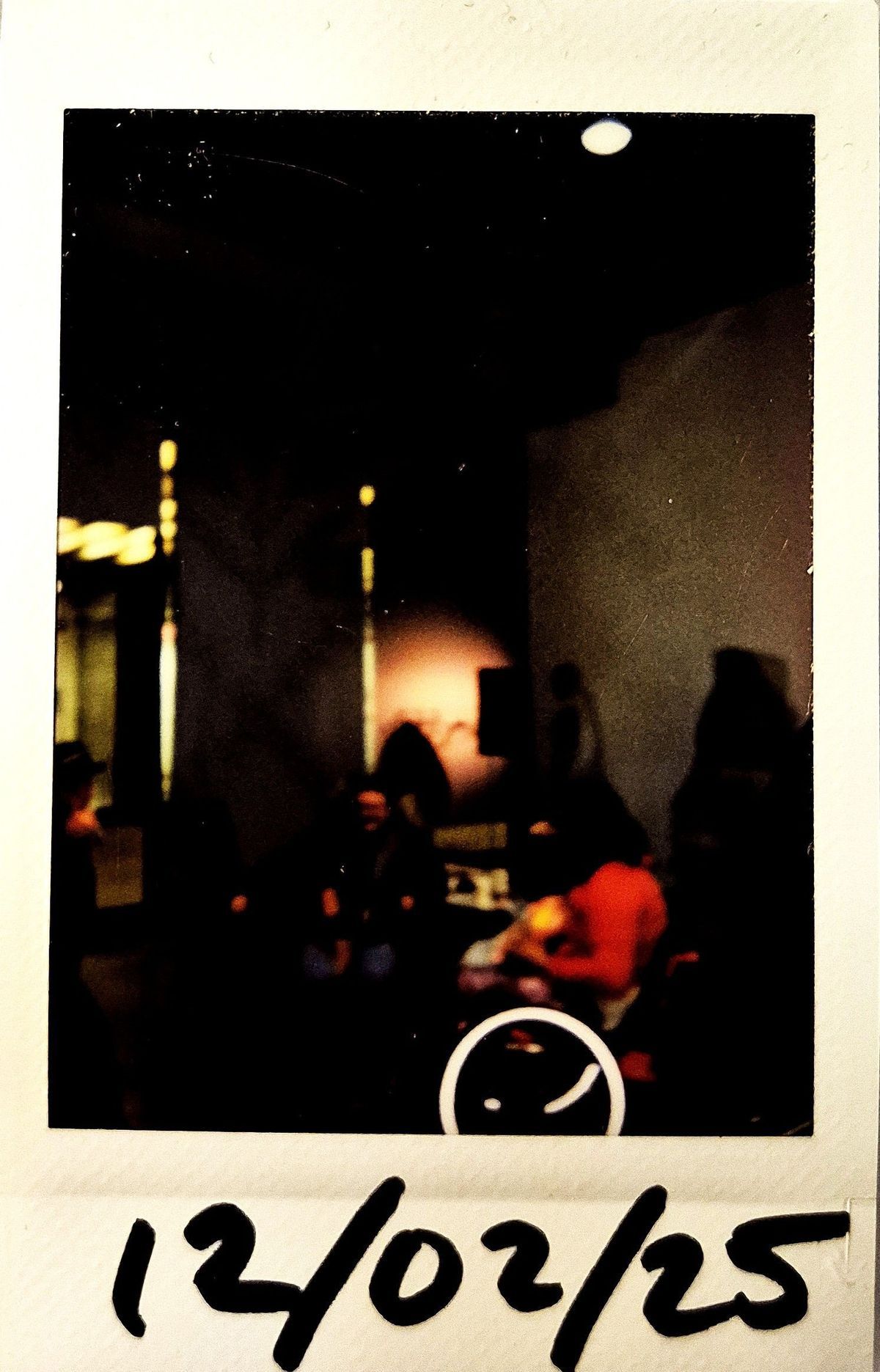 A dark lit polaroid which vaguely shows tables with people around them.