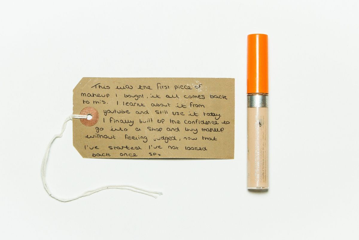 Clear tube of concealer with an orange top. There is a white label on the top left side and faded silver lettering across the bottom half of the tube.