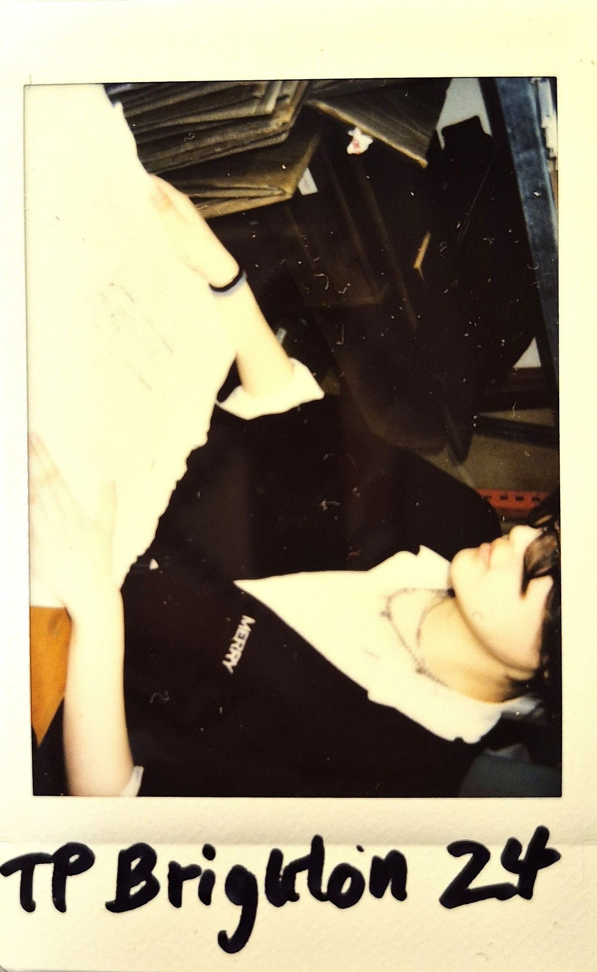 A person sits at a table, looking at something off-frame, wearing a dark apron.