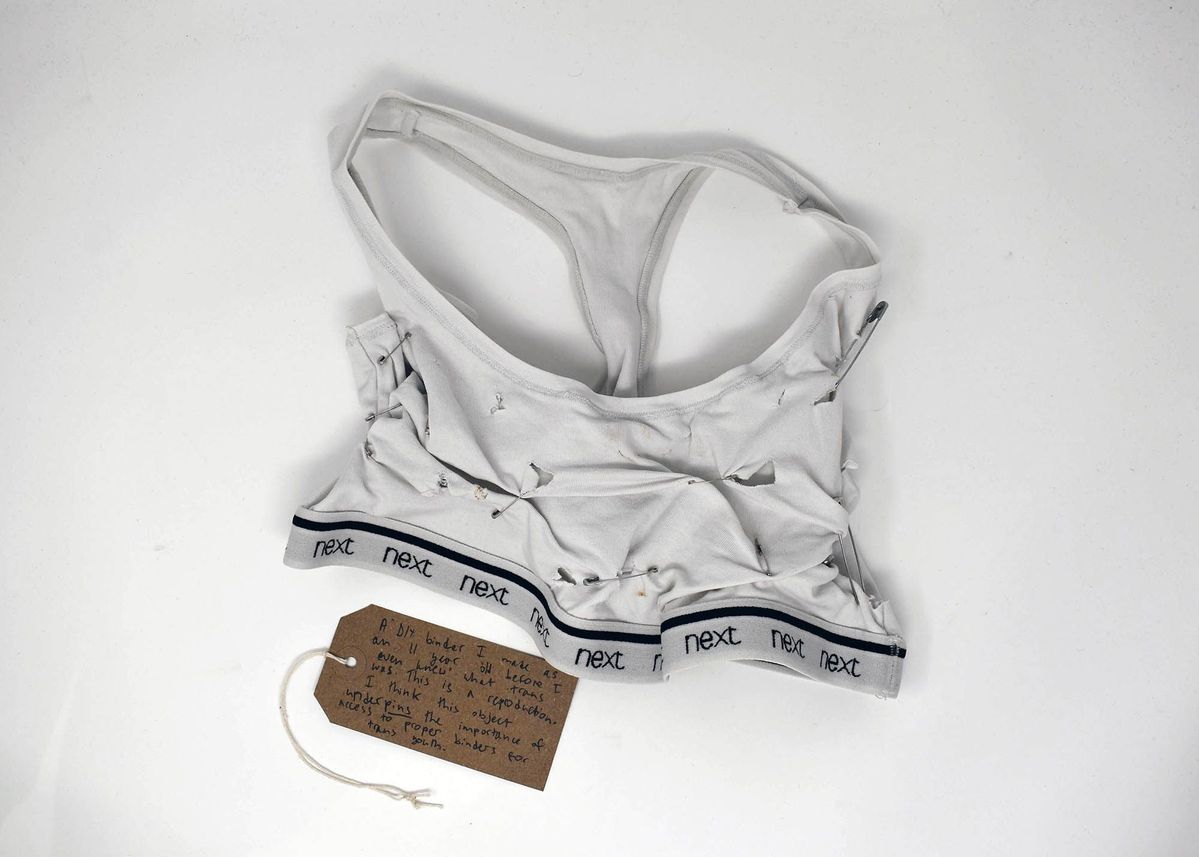 A homemade binder made from a tank top is displayed with visible safety pins and a note.