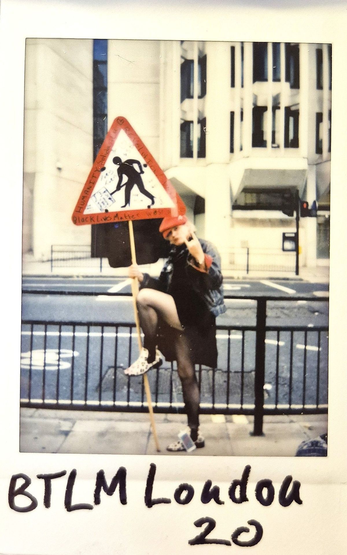 A person poses with a protest sign, wearing a red hat.