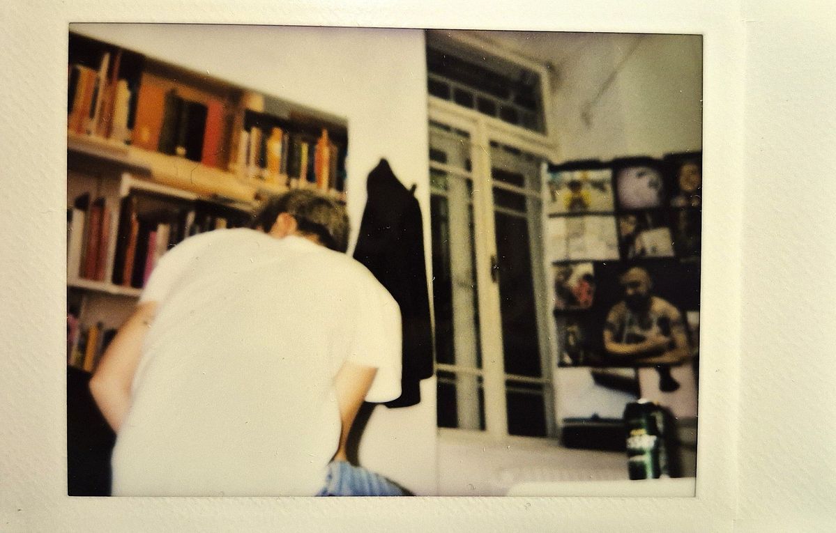 A person in a white shirt is sitting, facing shelves filled with books near a window.