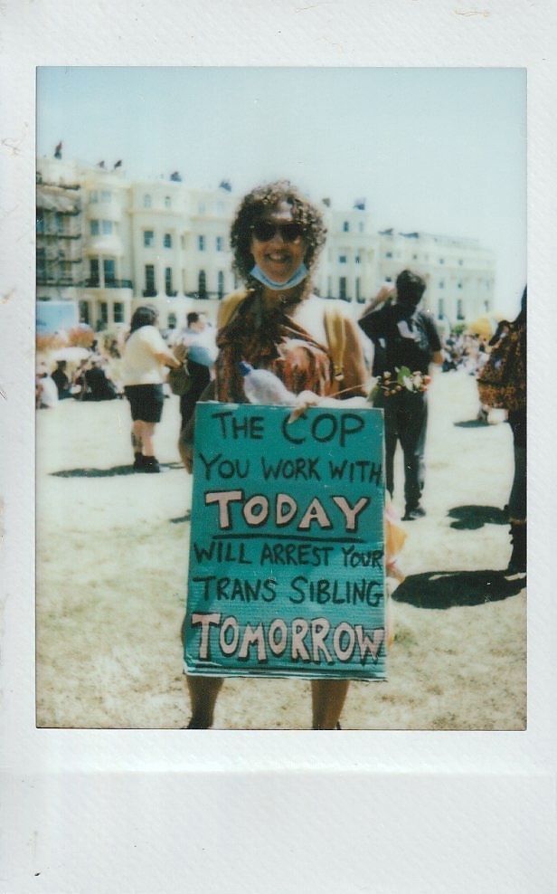 A person holds a sign saying, "The cop you work with today will arrest your trans sibling tomorrow".