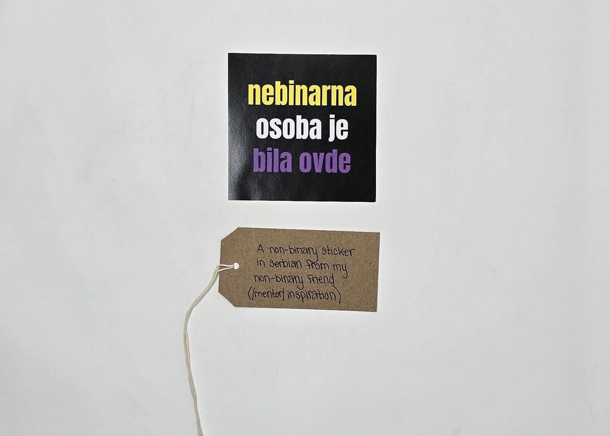 A non-binary sticker in Serbian. It has a black background with text in yellow, white and purple. With a brown, handwritten luggage tag.