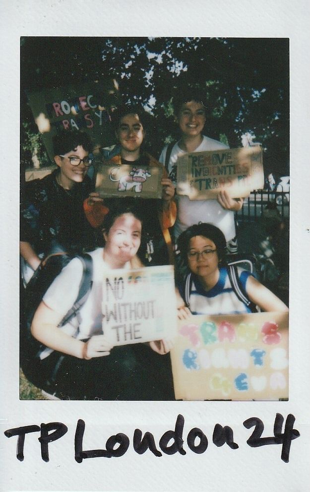 A group of five people are holding colorful signs advocating for trans rights and environmental issues.