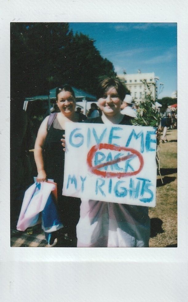 Two people stand together, one holding a sign that reads "Give Me My Rights."
