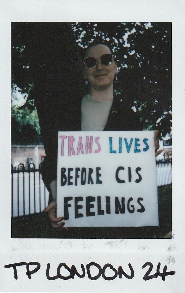 A person holds a sign reading "Trans Lives Before Cis Feelings" with "TP London 24" written at the bottom of the polaroid.