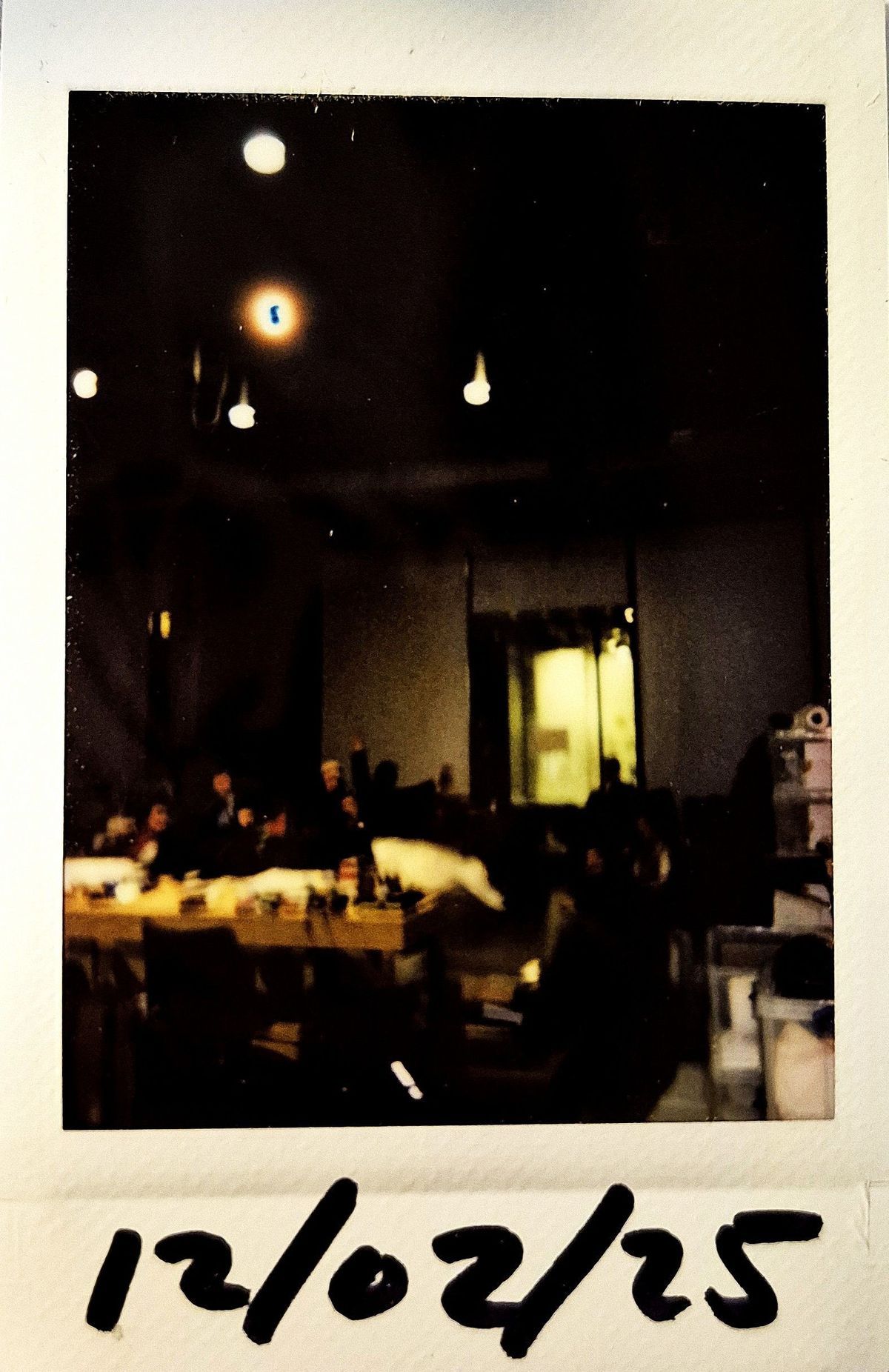 A dark lit polaroid which vaguely shows tables with people around them.