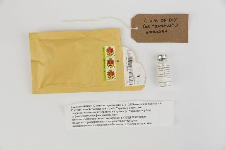 A vial of Estradiol with a padded envelope posted from Ukraine and a note in Cyrillic script. With a brown handwritten luggage tag.