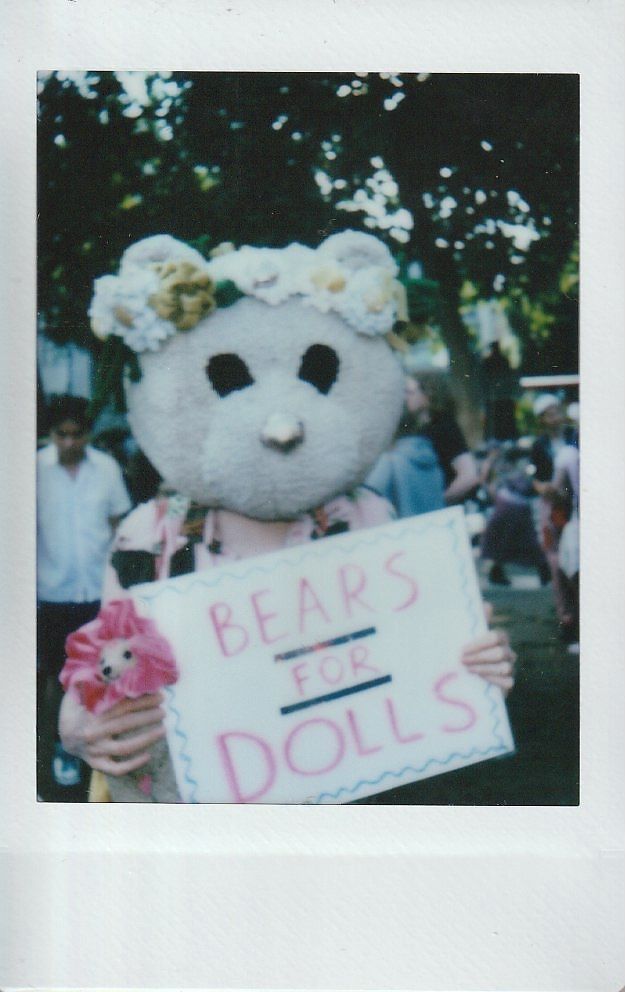 A person in a bear costume holds a sign reading "Bears for Dolls".
