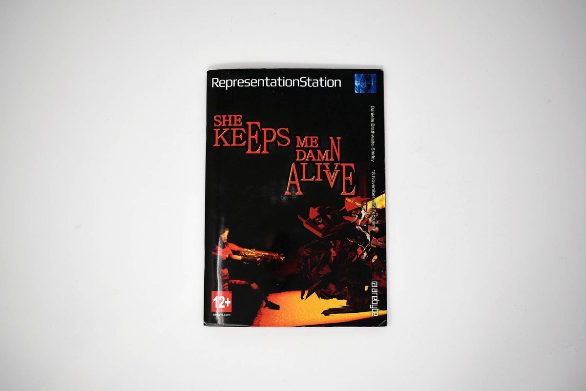 Black booklet reading "RepresentationStation" at the top with red letters reading "SHE KEEPS ME DAMN ALIVE" in jagged font underneath.