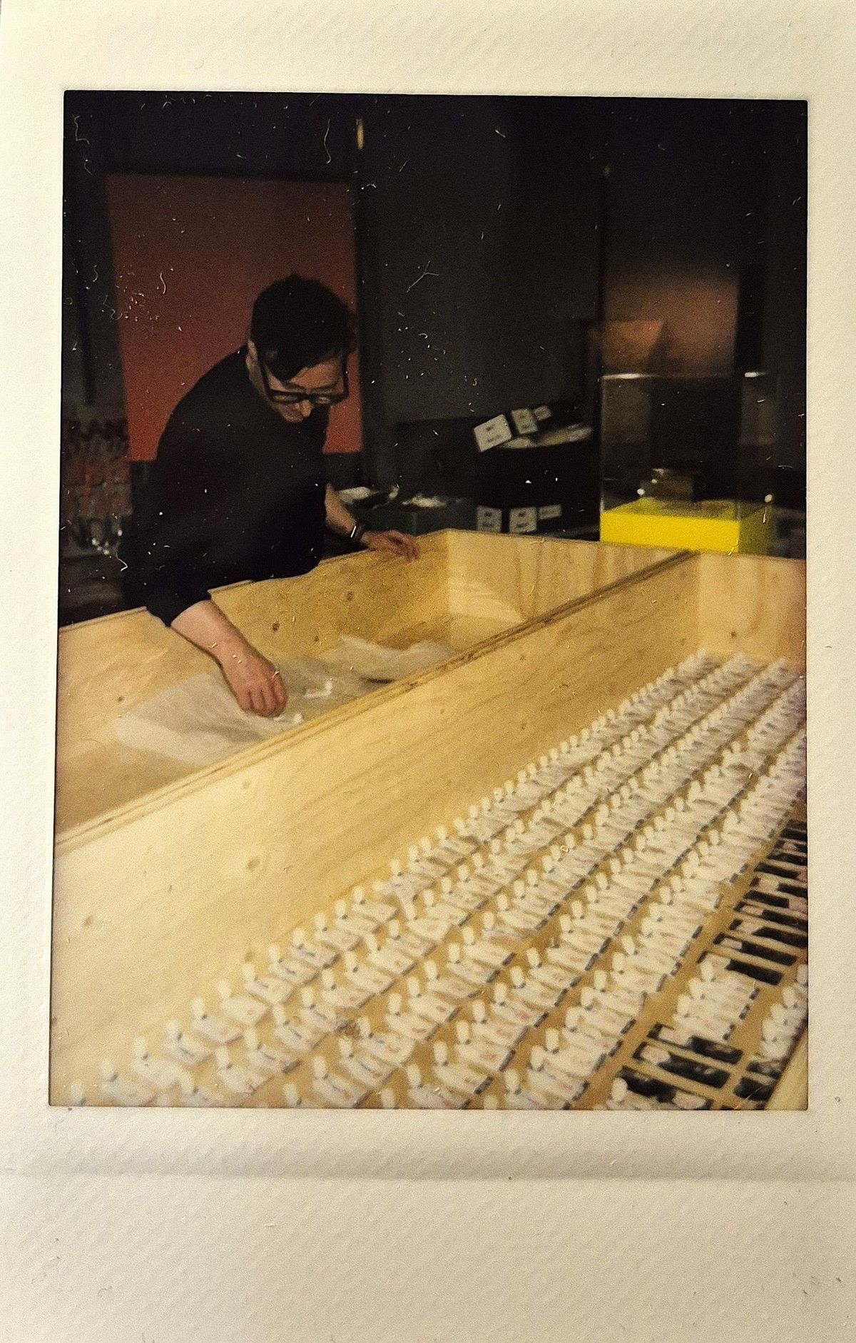 A person stands by a wooden box, preparing numerous small white objects in neat rows inside.