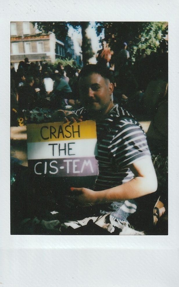 A person is holding a colorful sign that reads "CRASH THE CIS-TEM".