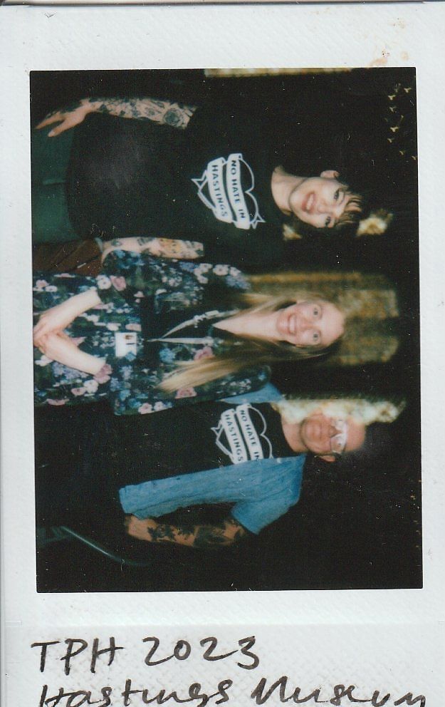 Three people are smiling in a group photo at Hastings Museum during an event in 2023.