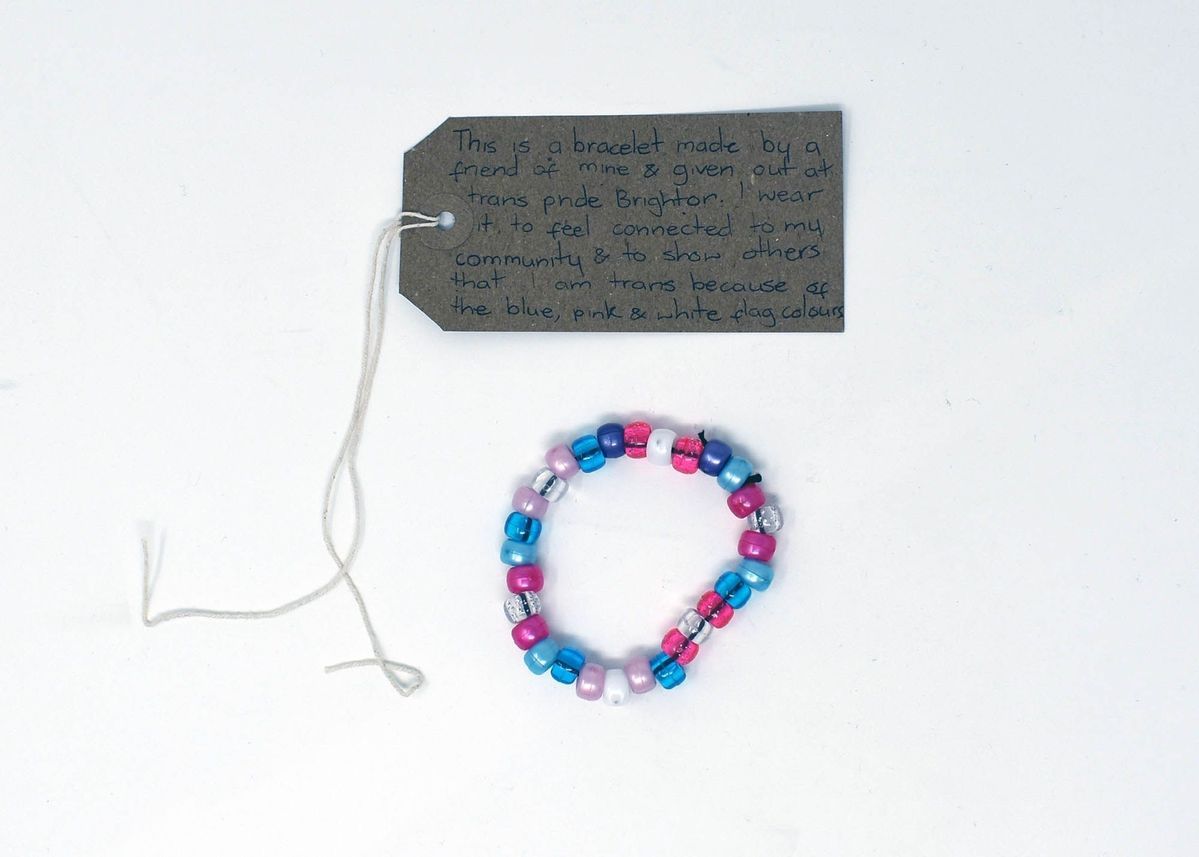 A bead bracelet made from blue, pink, white and clear beads. With a brown, handwritten luggage tag.