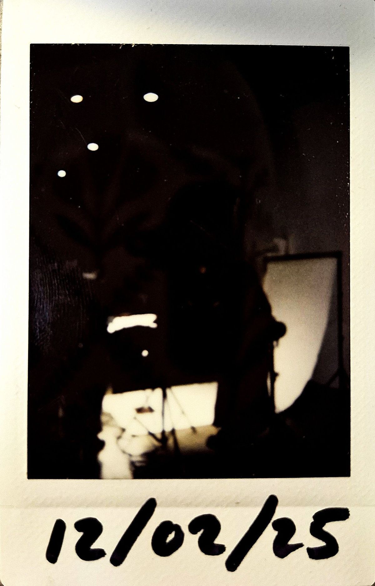 A dark lit polaroid which vaguely shows a photography lighting set up.