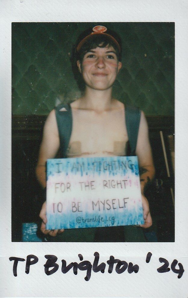 A person smiles while holding a sign advocating for the right to self-identity and expression.
