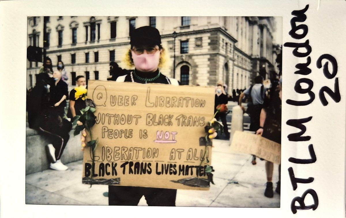 A person in a crowd holds a sign advocating for Black trans lives and queer liberation at a protest.