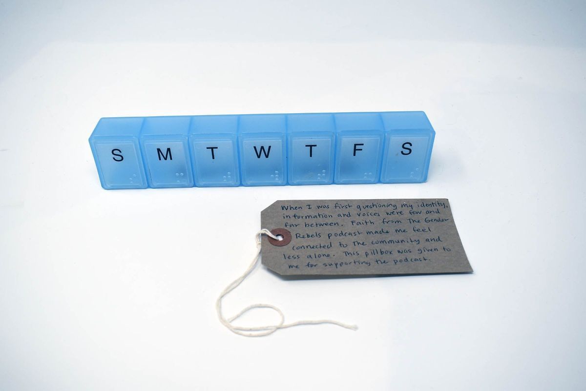 A transparent blue pill box that has seven compartments, labeled for the days of the week. With a brown, handwritten luggage tag.