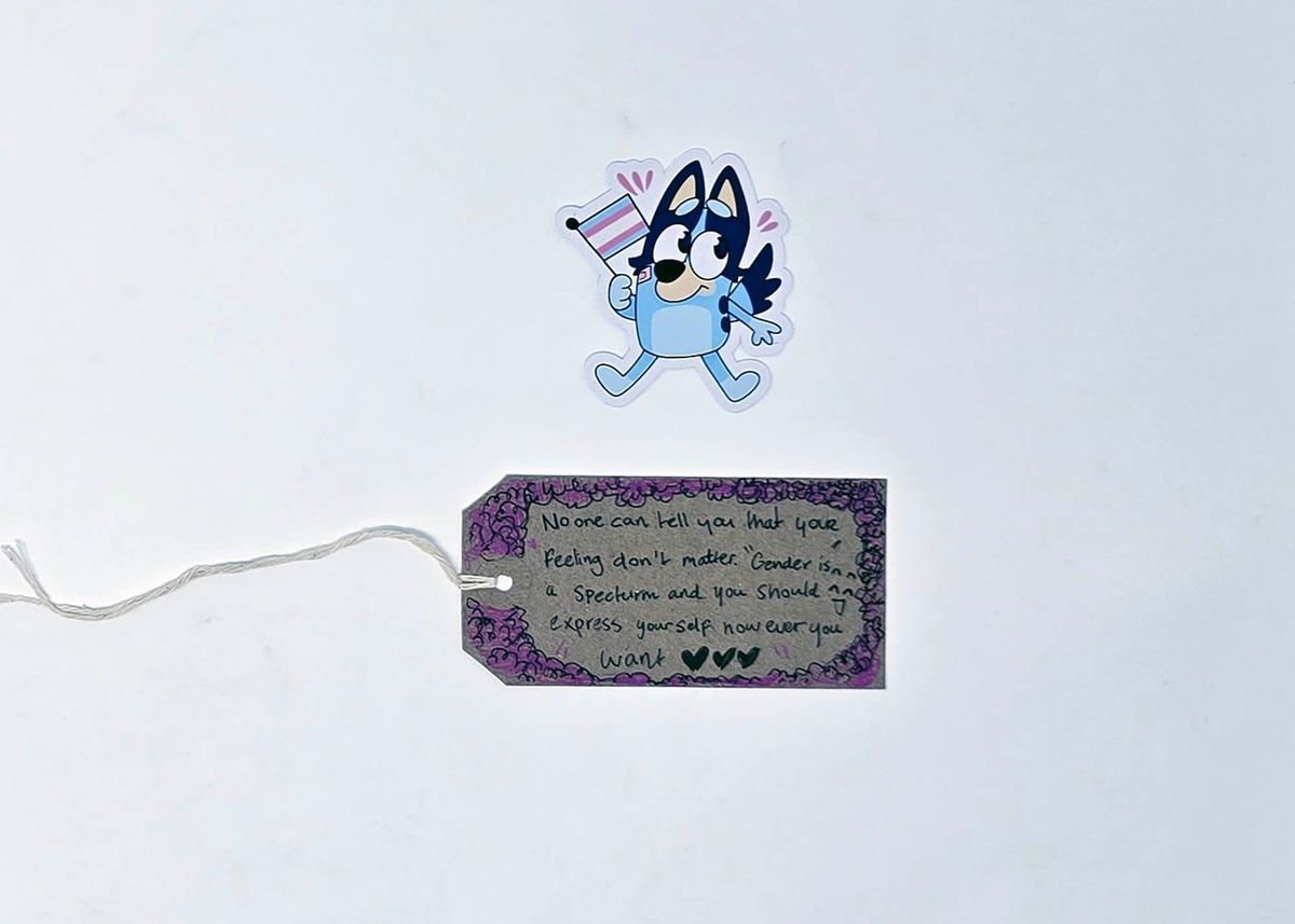 A cartoon character holds a flag above a tag with supportive, inclusive text and a decorative border.