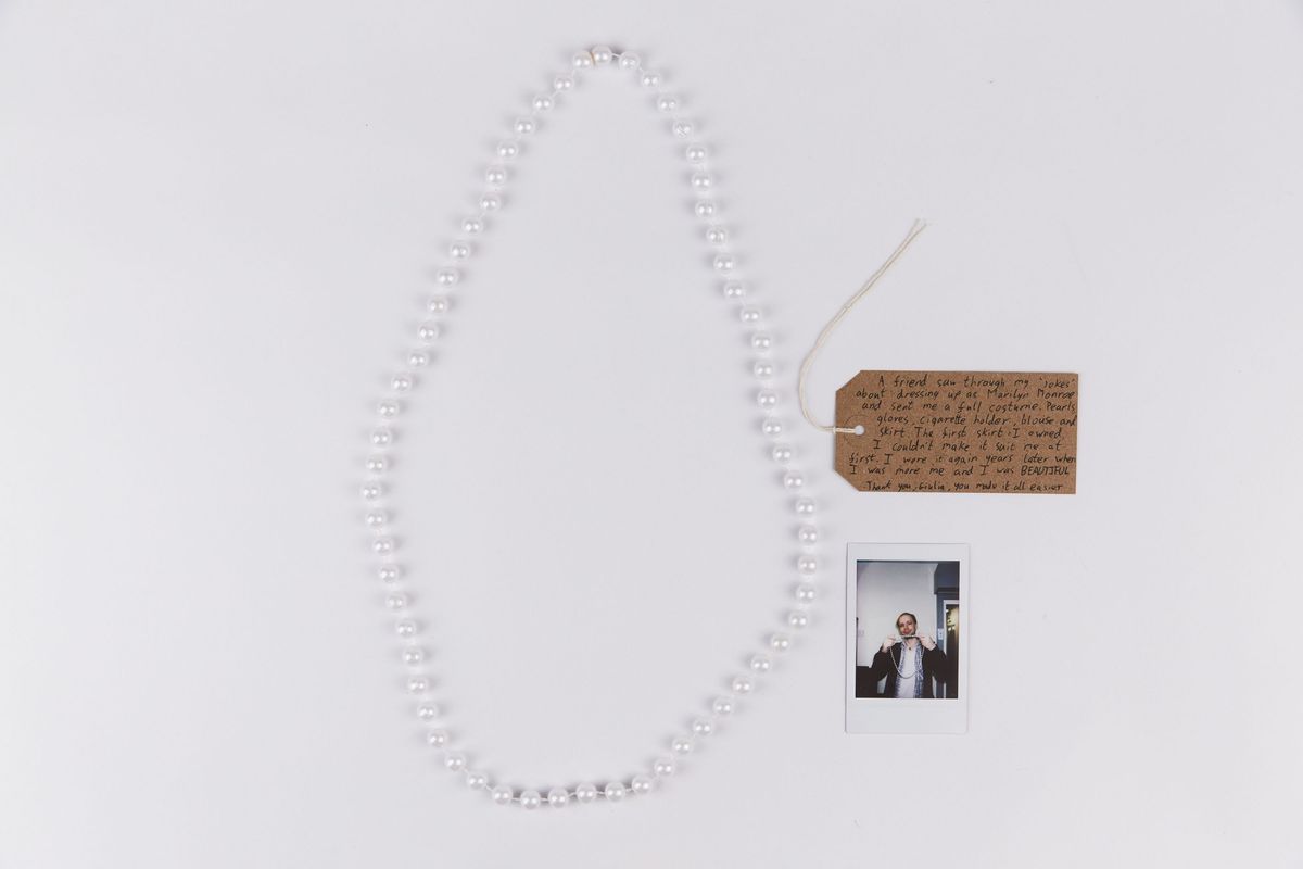 A pearl necklace, brown tag with writing on it and a polaroid of someone holding up the pearl necklace.