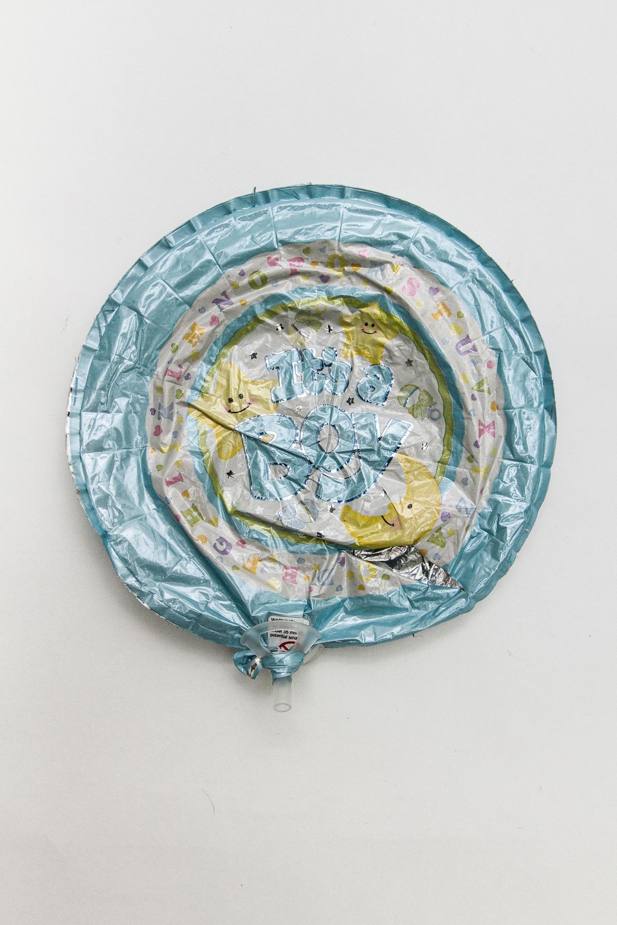 The image shows a deflated foil balloon with text “It's a Boy” designed with stars and alphabet