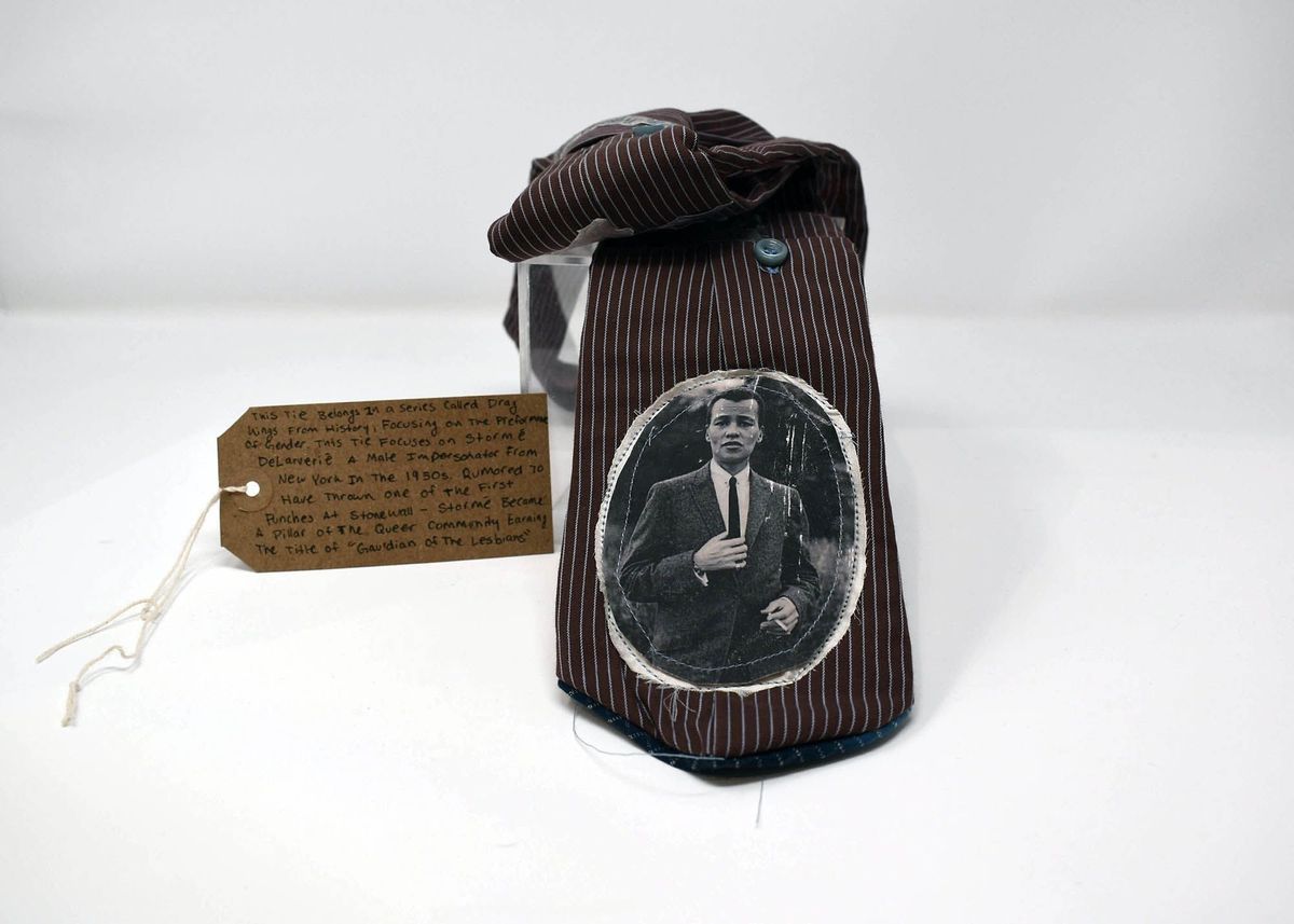 A brown, pinstripe tie featuring a picture of Stormé DeLarverié. With a brown, handwritten luggage tag.