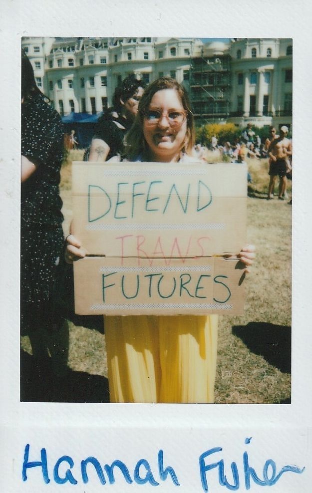 A person in glasses holds a sign reading "Defend Trans Futures" at an outdoor event.