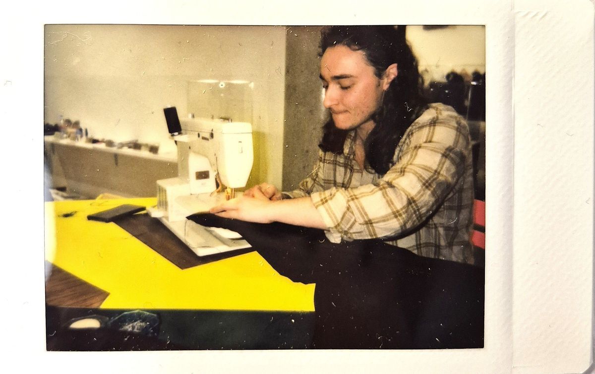 A person wearing a plaid shirt is sewing fabric on a white sewing machine indoors.