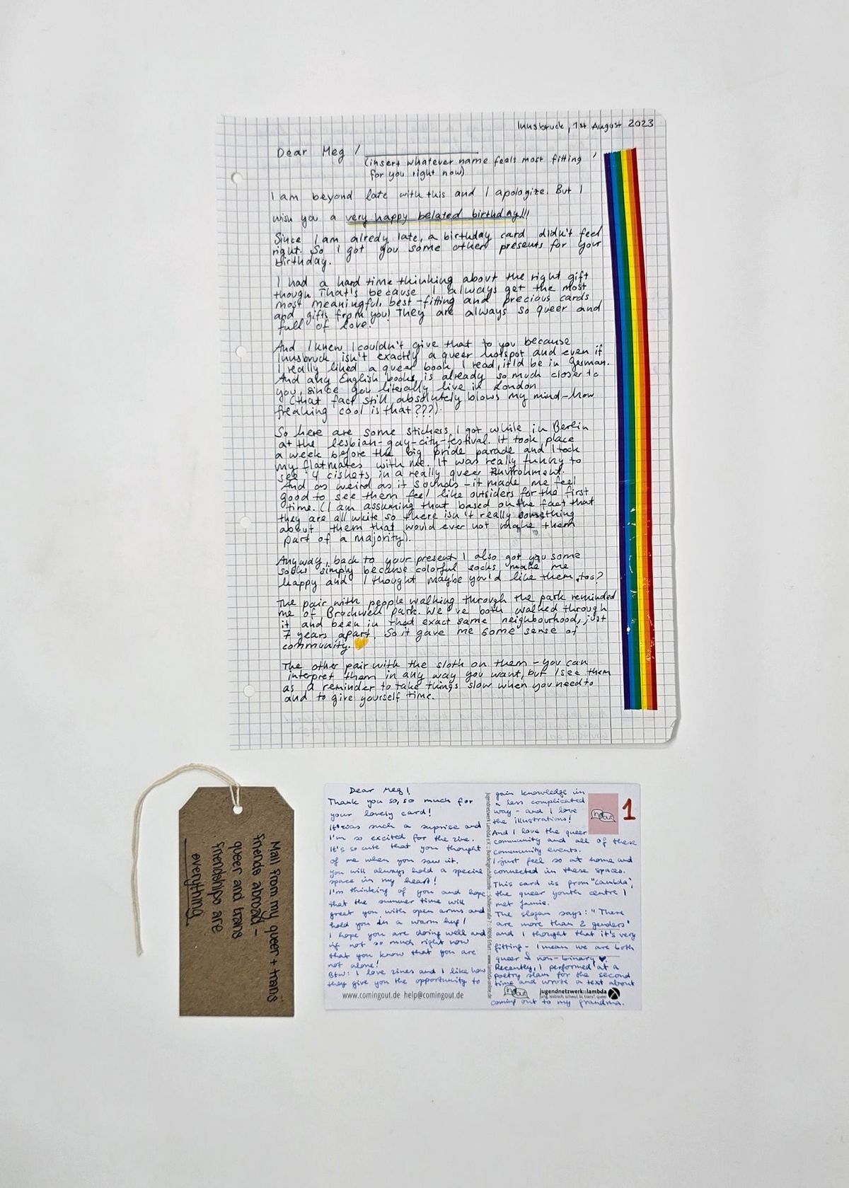 A letter, written on squared paper highlighted with rainbow tape, and a postcard. Both to Meg. With a brown, handwritten luggage tag.