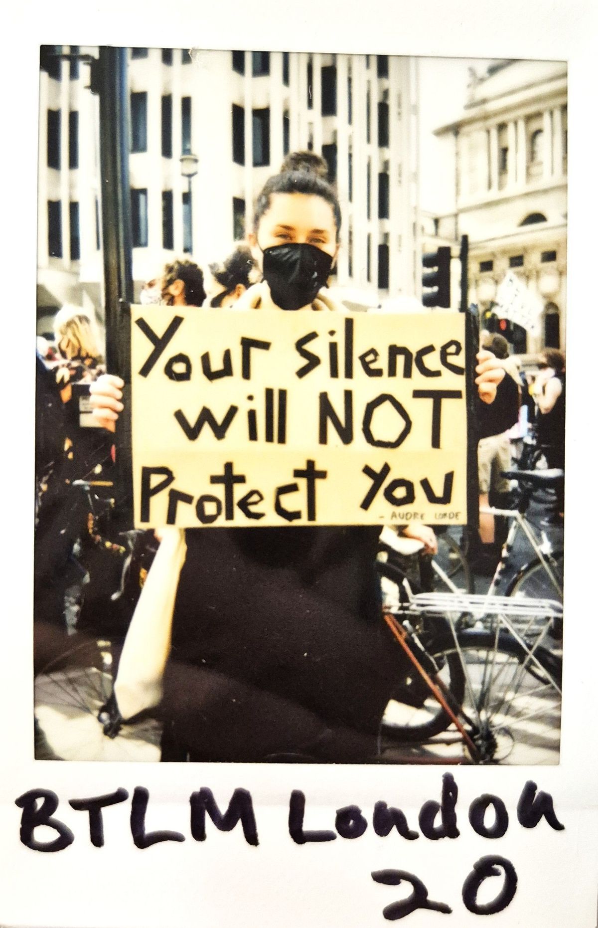 A masked protester holds a sign reading, "Your silence will NOT protect you," at a demonstration
