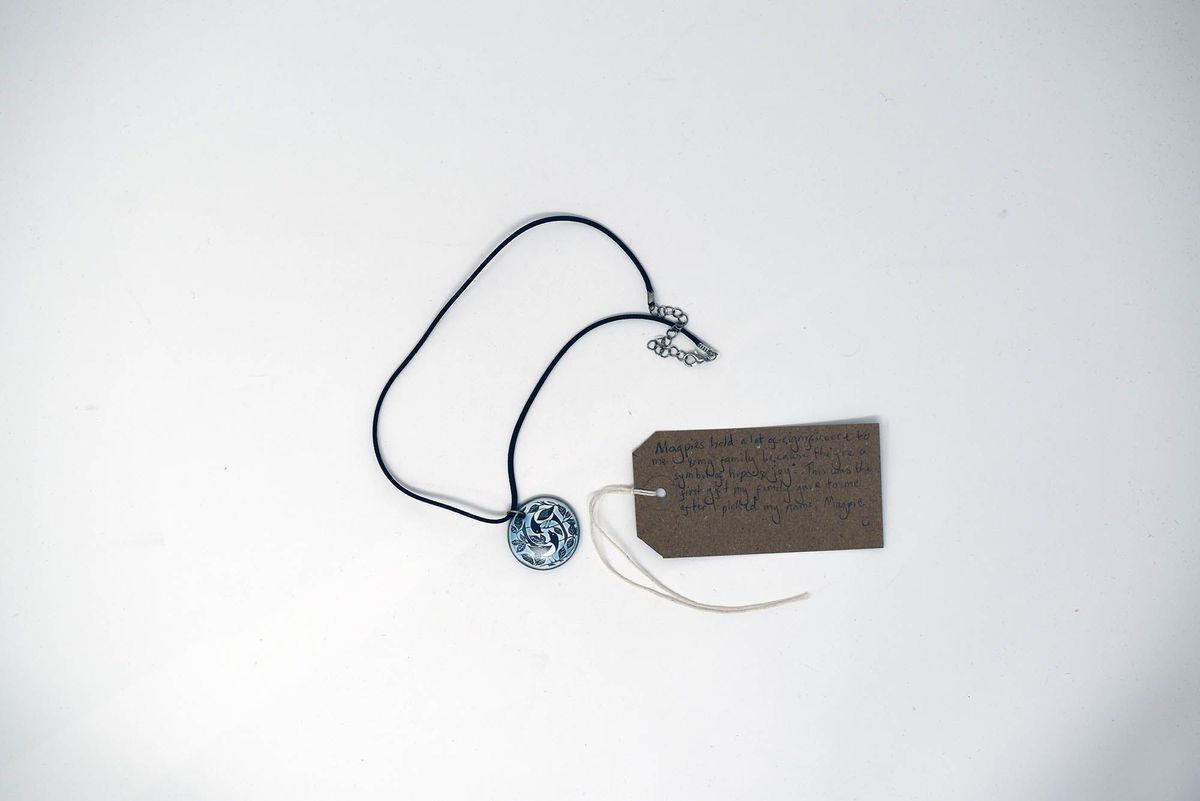 A necklace with a circular pendant lies beside a brown tag with handwritten text.