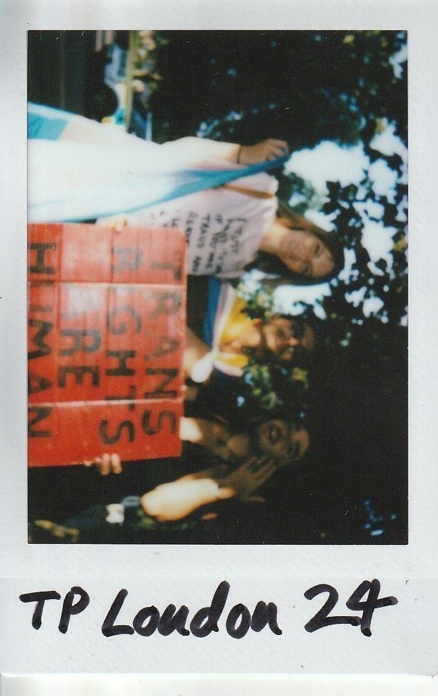 The image shows people holding a sign reading "Trans Rights are Human Rights." They are outdoors.