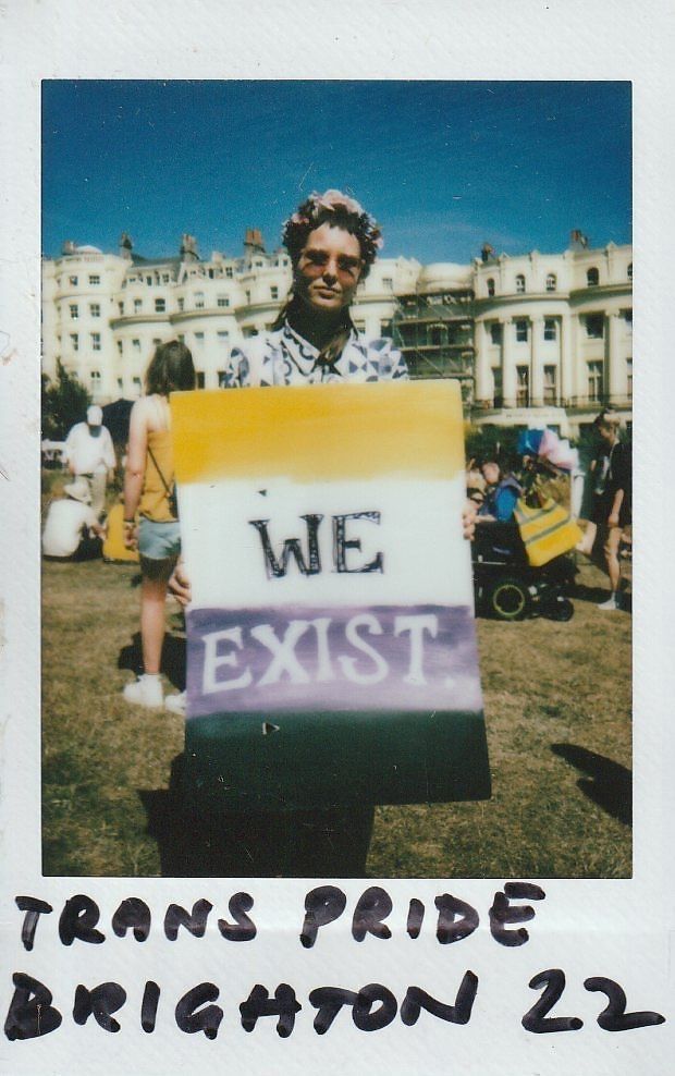 A person proudly holds a sign reading “We Exist” at a Trans Pride event in Brighton.
