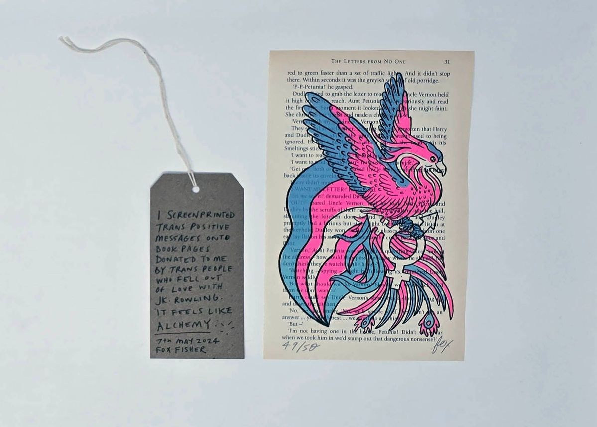 A page from a Harry Potter book shows a colorful phoenix drawing in trans flag colours with a tag describing the artwork’s trans-positive message.