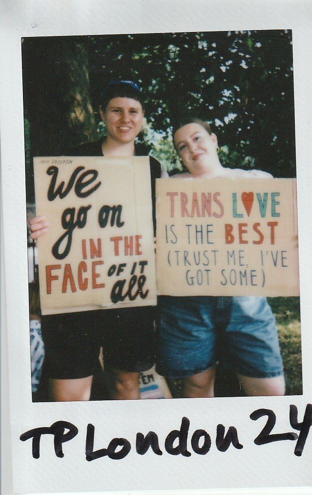 Two people are holding signs with supportive messages, standing together in an outdoor setting.