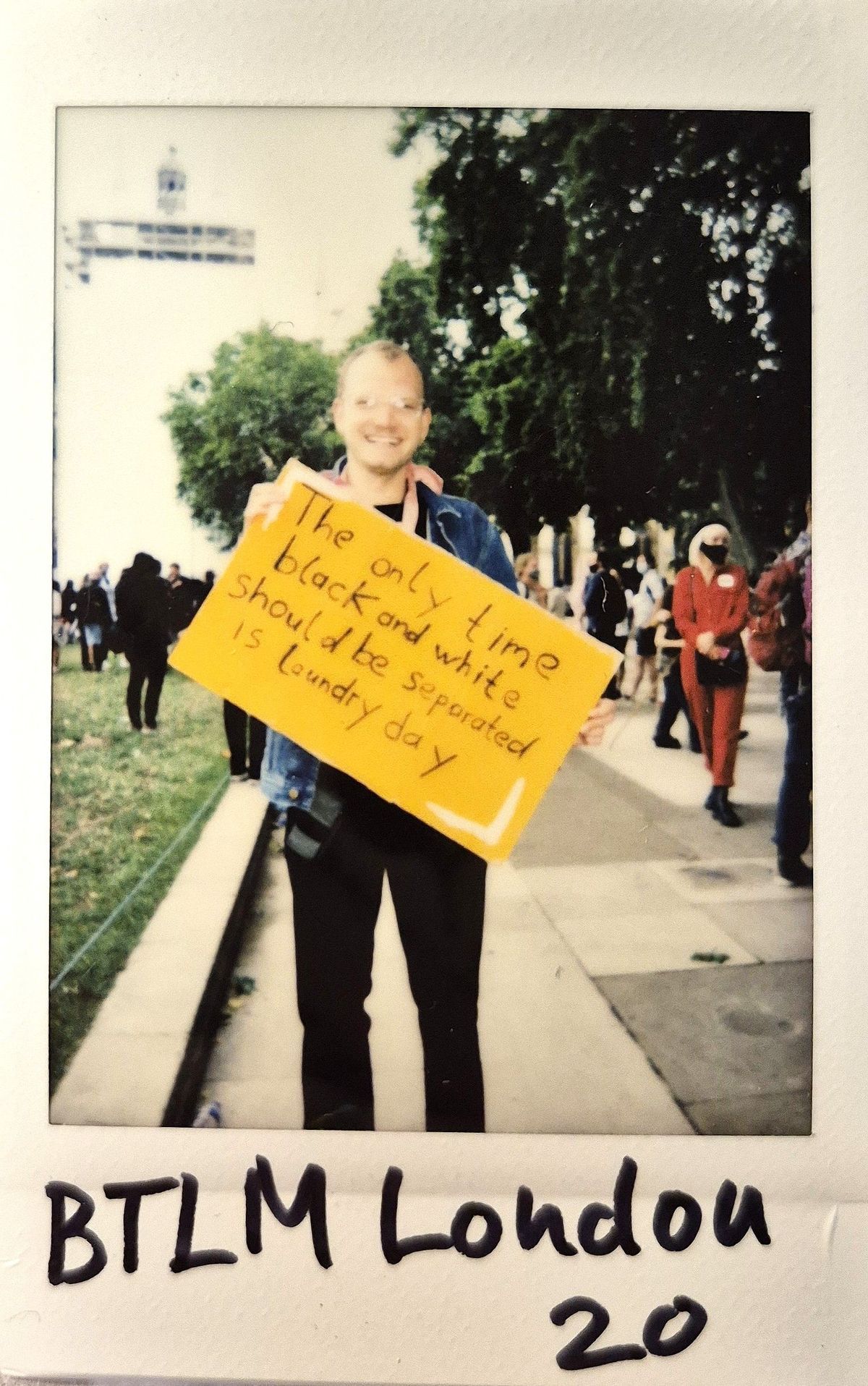 A person holds a sign advocating equality, surrounded by others, in an outdoor setting with trees.