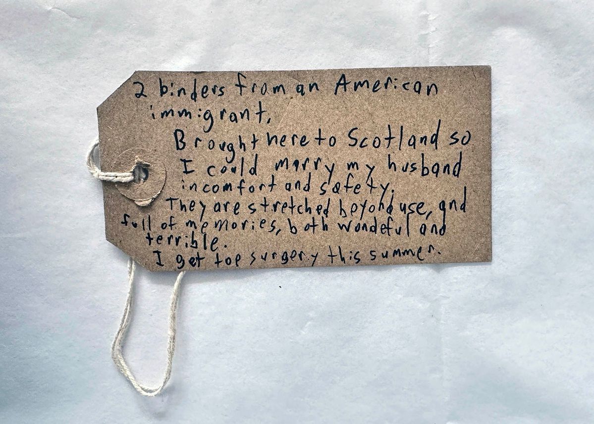 A handwritten note on a brown tag shares a personal narrative about binders and top surgery.