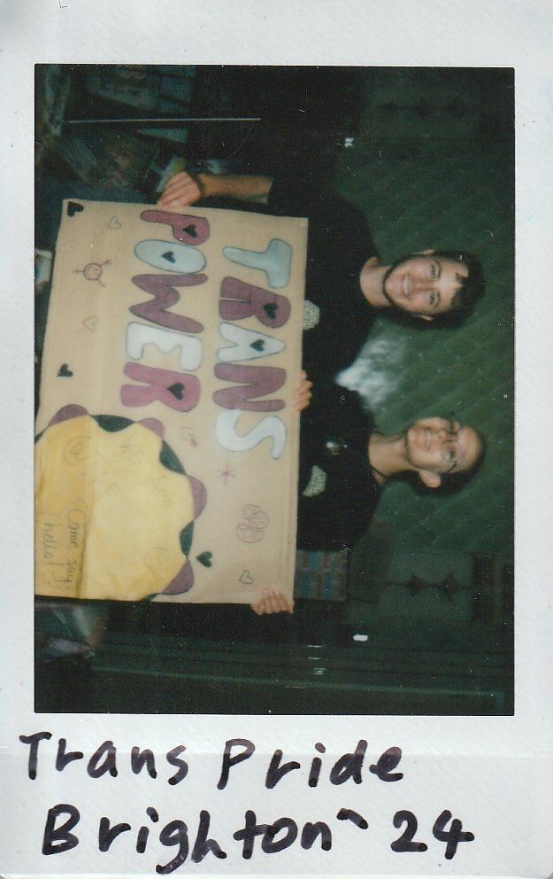 Two people happily hold a colorful "Trans Power" sign at the Trans Pride event in Brighton.