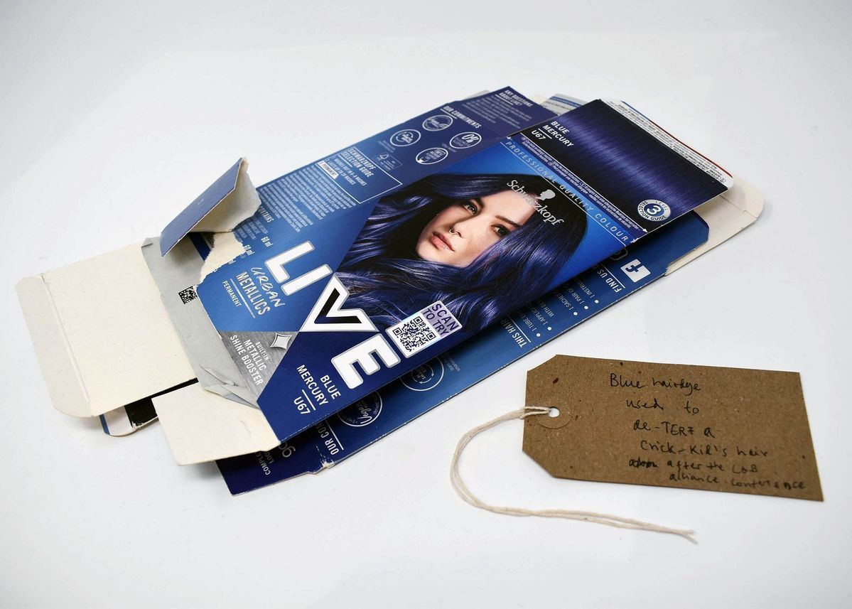 Two empty, flattened boxes of Schwartzkopf Urban Metallics Blue Mercury hair die. With a brown, handwritten luggage tag.