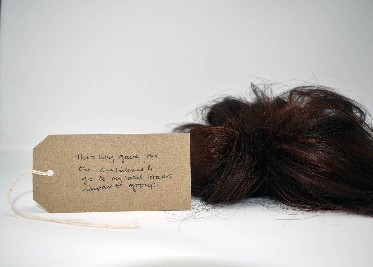 A dark brown wig with a brown handwritten luggage tag.