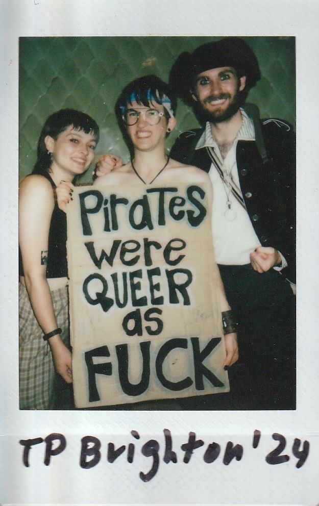 Three people pose for a photo, holding a bold sign about pirates.