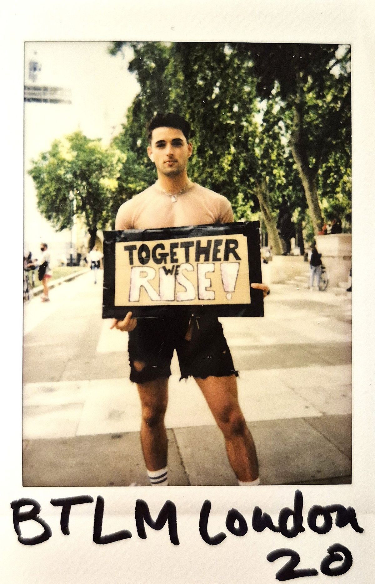 A person stands on a street holding a sign that reads, "TOGETHER WE RISE!"