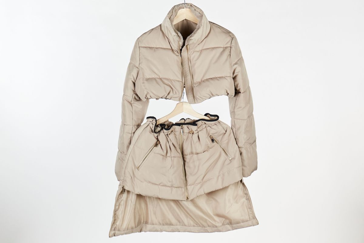A beige, quilted jacket and matching skirt are hanging on a wooden hanger.