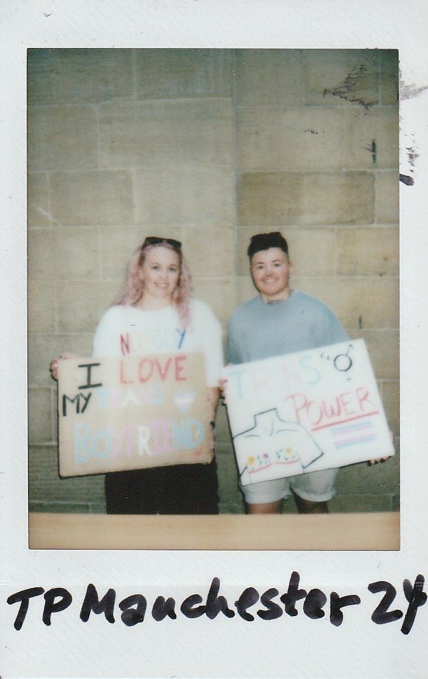Two people smiling while holding colorful signs at an event.