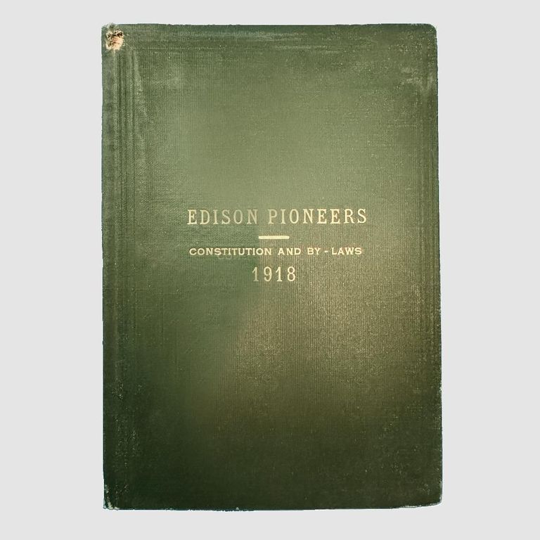 Front cover of the Edison Pioneers Constitution and By-Laws, 1918, a publication detailing the foundational principles, regulations, and structure of the Edison Pioneers organization.; The image depicts a vintage book with a dark green cover, featuring the title 