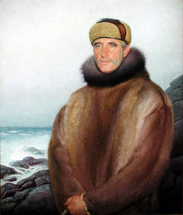 Portrait of a man in hat and fur coat, standing in front of rocky shoreline