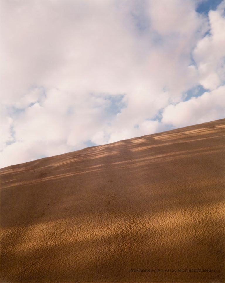 Photograph of sandy dune with blue sky and clouds in the background