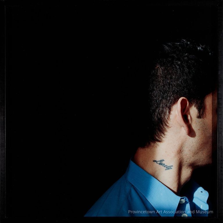 Person's head in profile, mostly in shadow, eyes not visible, wearing blue shirt with "Lonely" tattooed on their neck