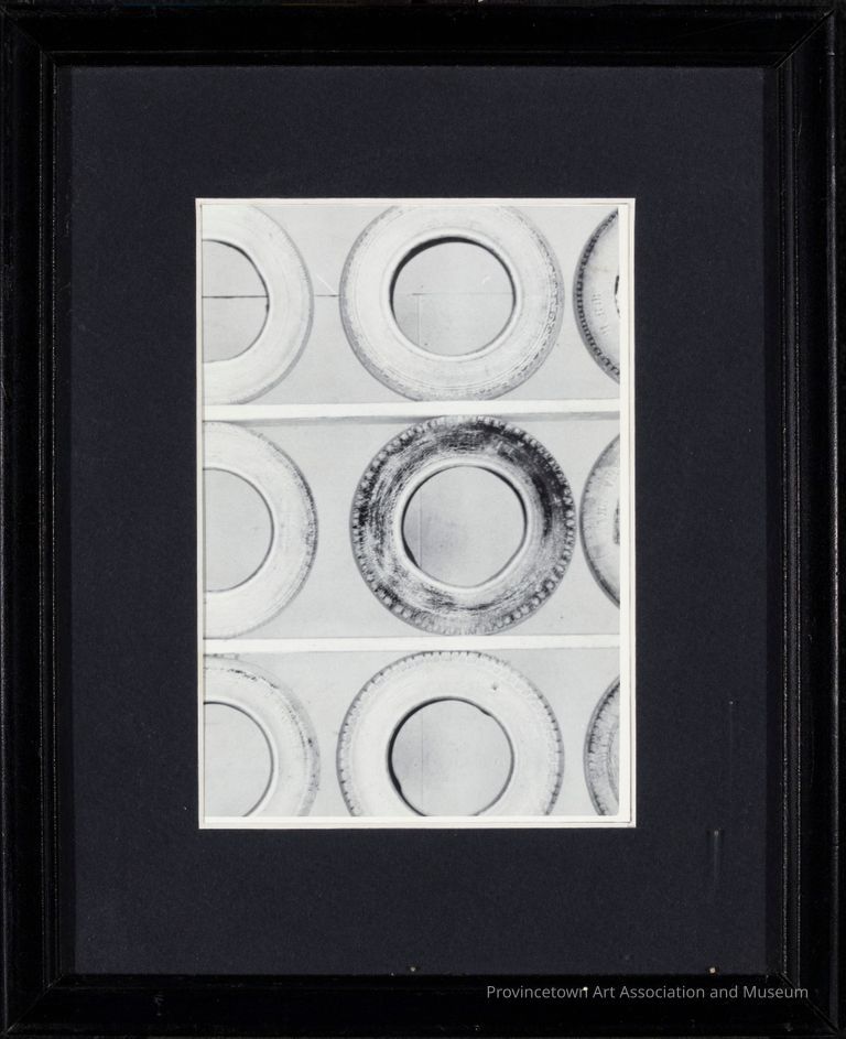 A black and white photograph captures  nine tires placed on shelves. With the circles facing out, three white painted tires are assigned to each shelf.